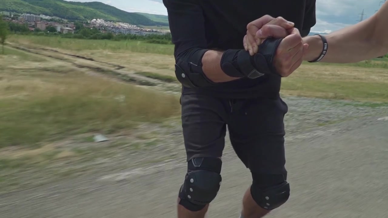 Zwei Männer fahren gemeinsam Inlineskates, Händchen haltend auf einem malerischen Weg mit Hügeln im Hintergrund