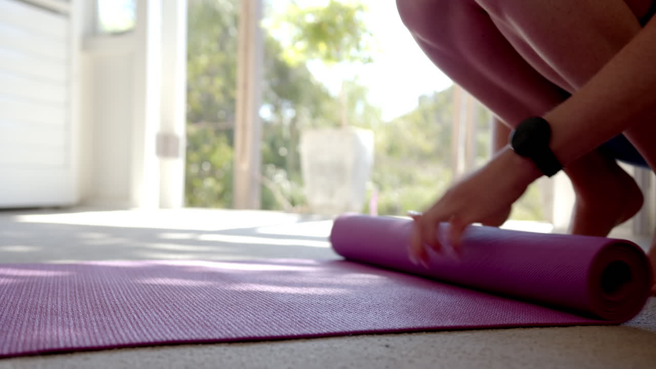 Rolling up yoga mat, woman finishing home workout in bright living room, copy space