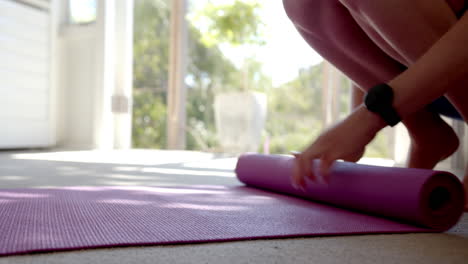 rolling up yoga mat, woman finishing home workout in bright living room, copy space