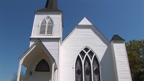 the white clapboard exterior of an old country church is set against a blue sky in this panning shot