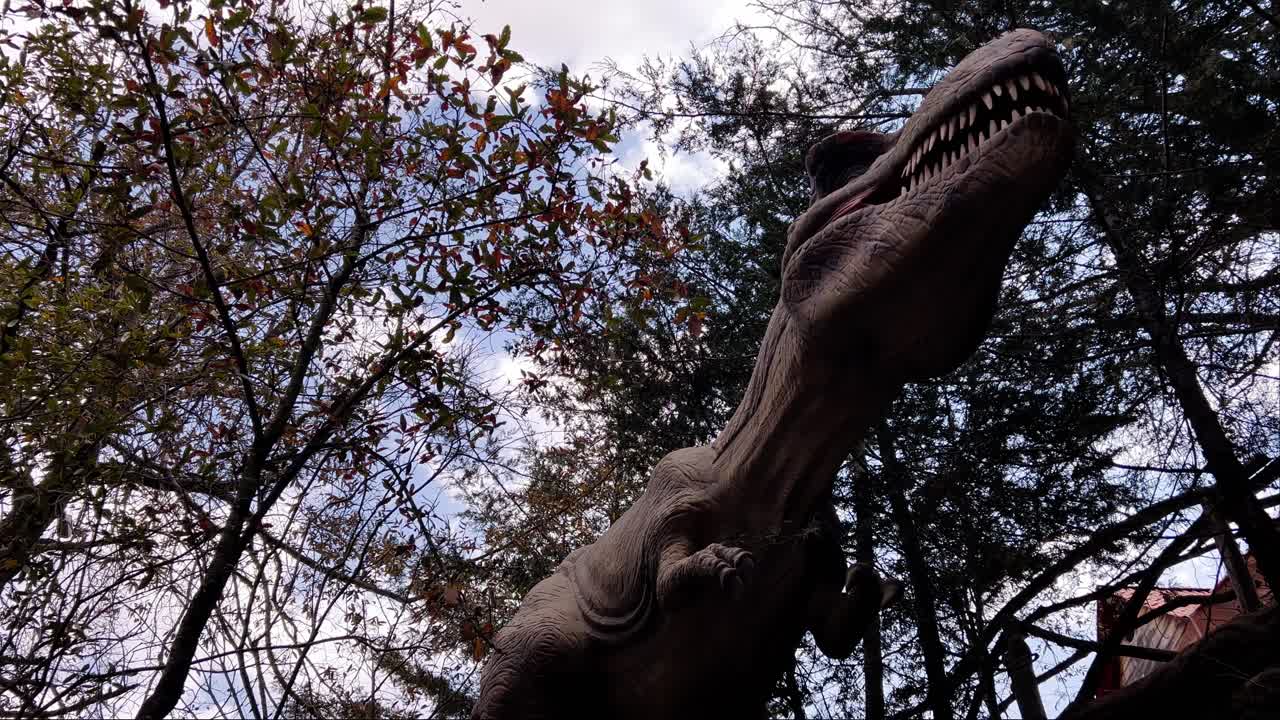 A towering dinosaur sculpture peeks through trees, offering a dramatic perspective of nature.