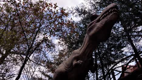 a towering dinosaur sculpture peeks through trees, offering a dramatic perspective of nature.