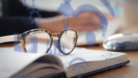 animation of technology icons over, book, glasses and hands of caucasian man typing on keyboard