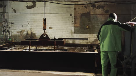 trabajador industrial en el panel de control supervisando el tanque de extinción con gancho de grúa en una fábrica de vintage