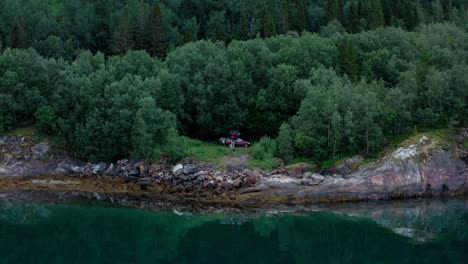 a person with a car roof tent amidst dense trees by the lakeshore