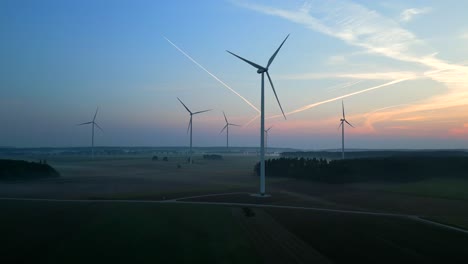 Drone-camera-flying-over-a-flat-landscape-in-the-morning-sun-slowly-approaches-a-wind-turbine-farm