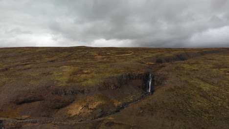 Imágenes-Aéreas-Que-Se-Mueven-Hacia-Una-Cascada-Ubicada-En-Las-Tierras-Altas-De-Las-Montañas-De-Islandia