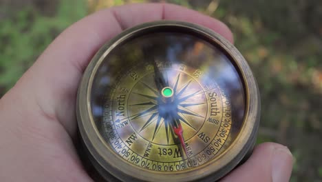 traveler hand holds a old directional compass in summer forest. person use compass to find location. travel concept close-up.