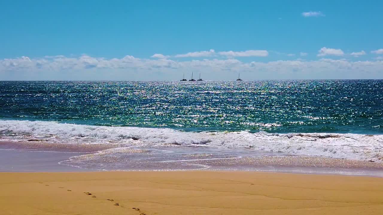 hd 하와이 카우아이 백라이트 슬로우 모션 스태틱 와이드 샷 반짝이는 파도가 해변에서 씻어내고 4개의 보트 중 두 번째 보트가 부분적으로 흐리고 푸른 하늘이 있는 프레임 중앙 근처에서 첫 번째 보트를 통과합니다.