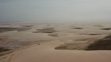 aerial: a truck with kitesurfers traveling through the dunes of lencois maranhenses in brazil, during dry season