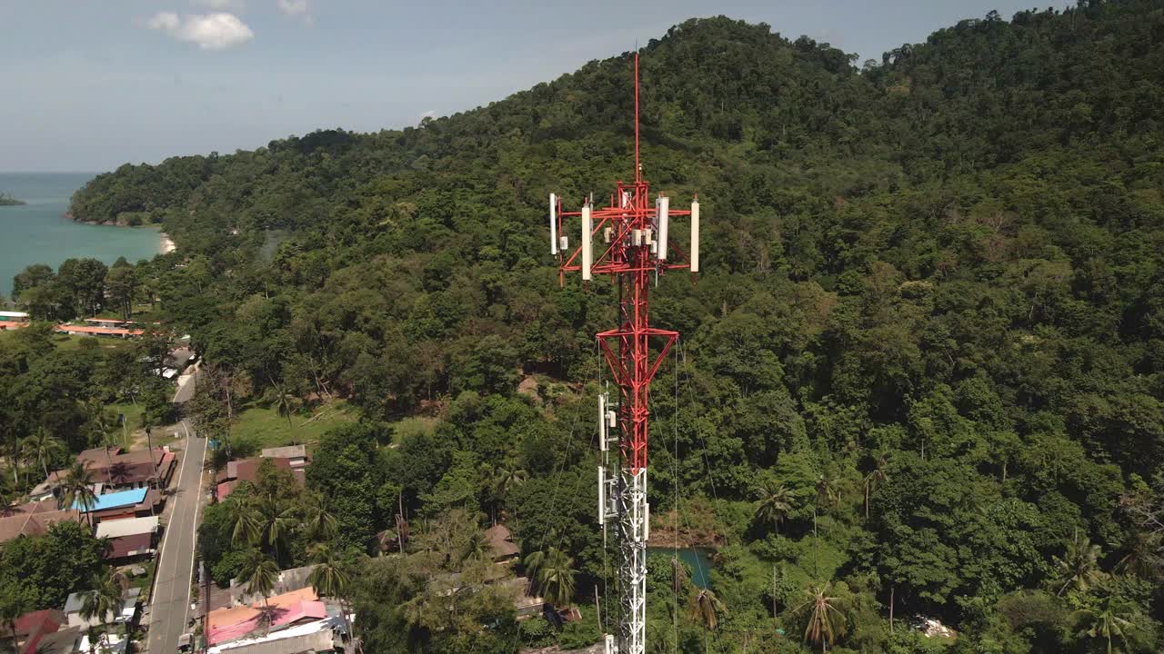 toma aérea de un dron de órbita lenta de una torre de telecomunicaciones roja y blanca en una isla tropical en tailandia con selva, vista al mar e islas