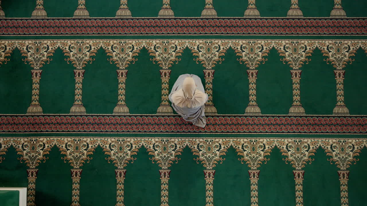 A Muslim woman prays on a green carpet in a mosque