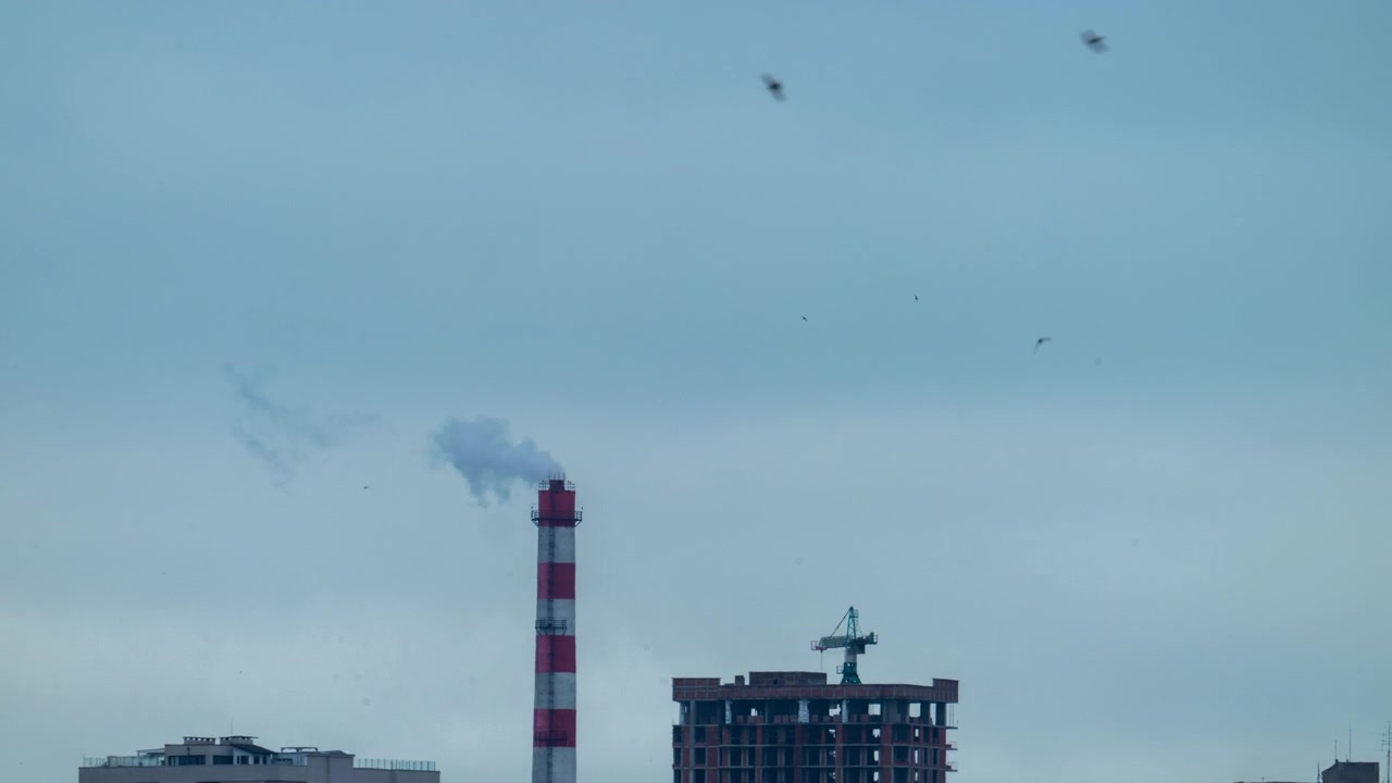 Timelapse af en stribet industriel skorsten, der udleder damp over en bysilhuet.