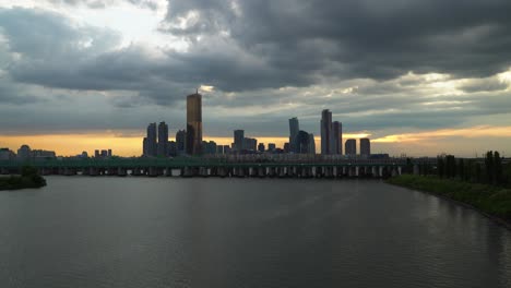 Trains-Passing-By-The-Railway-Bridge-Over-Han-River-Background-With-Tall-Buildings-At-Sunset