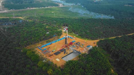 cinematic onshore drilling and workover rig structure and rig equipment for oil exploration and exploitation in the middle of jungle surrounded by palm oil trees during sunset time.