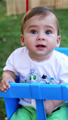 baby boy swaying in the swing hanging in the garden. spending summer in the nature. view from above. blurred backdrop. vertical video