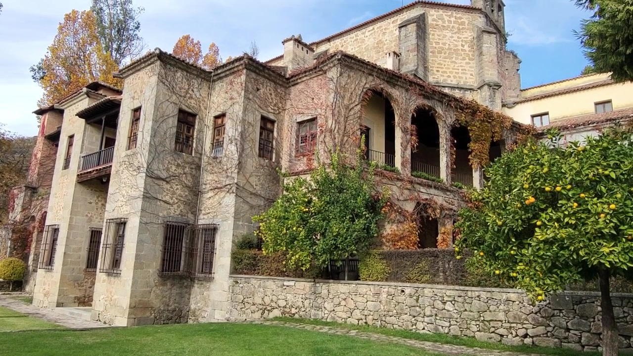 Monasterio de Yuste. Fachada principal del monasterio, con una espadaña y vegetación cubriendo los muros y arcos. Yuste, España