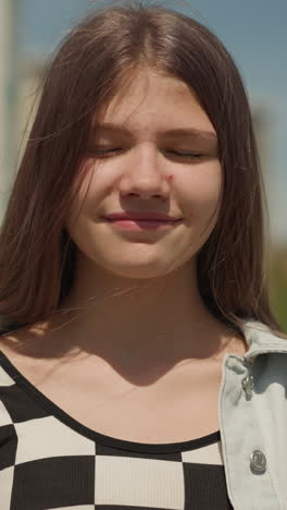 girl stands near high-rise building closing eyes dreamily. teenager fantasizes about ancient heroic events smiling happily closeup on blurred background