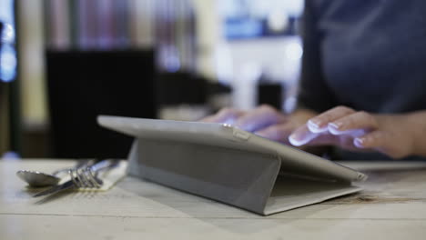 mujer en un café usando una tableta para enviar un mensaje