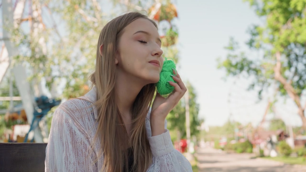 Primo piano di una giovane donna che tiene ed esamina filato verde in un ambiente di parco all'aperto con alberi, luce diurna soffusa e dettagli dello sfondo sfocati. Il soggetto maneggia filato dai colori vivaci