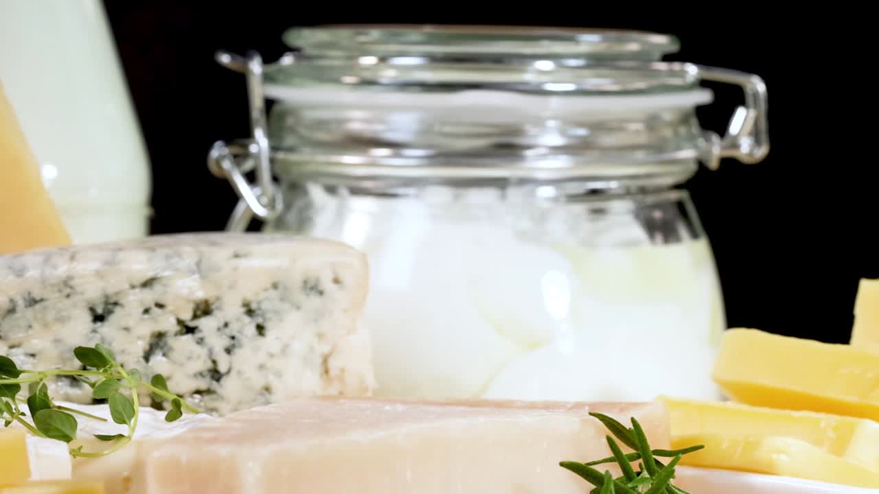 A variety of cheeses and yogurt jars arranged neatly with herbs on a black background.