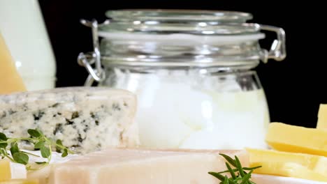a variety of cheeses and yogurt jars arranged neatly with herbs on a black background.