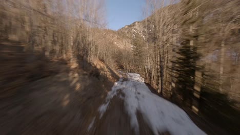 dron fpv volando a lo largo de un camino forestal hasta las montañas austriacas con una cascada congelada al atardecer
