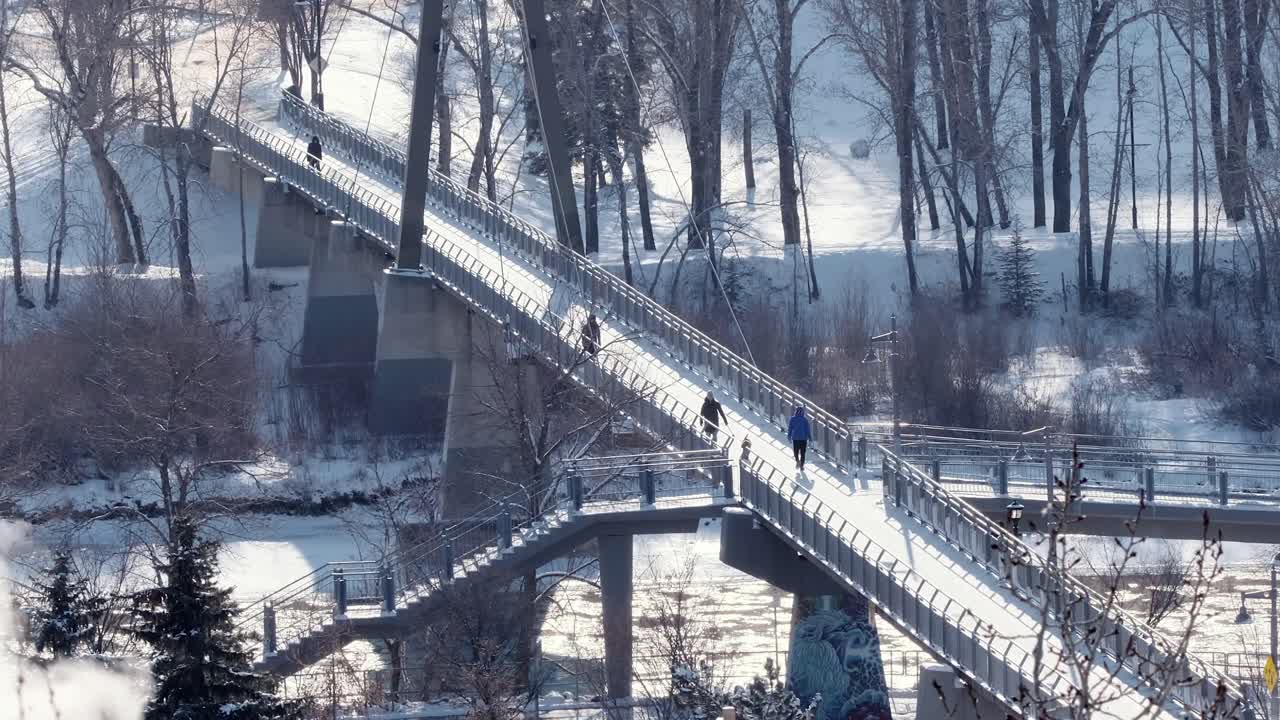 People Walking on a Snowy Bridge Over a River in Winter