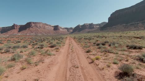 FPV-aerial-following-path-over-Indian-Creek-desert-towards-huge-cliffs-in-background-on-sunny-day