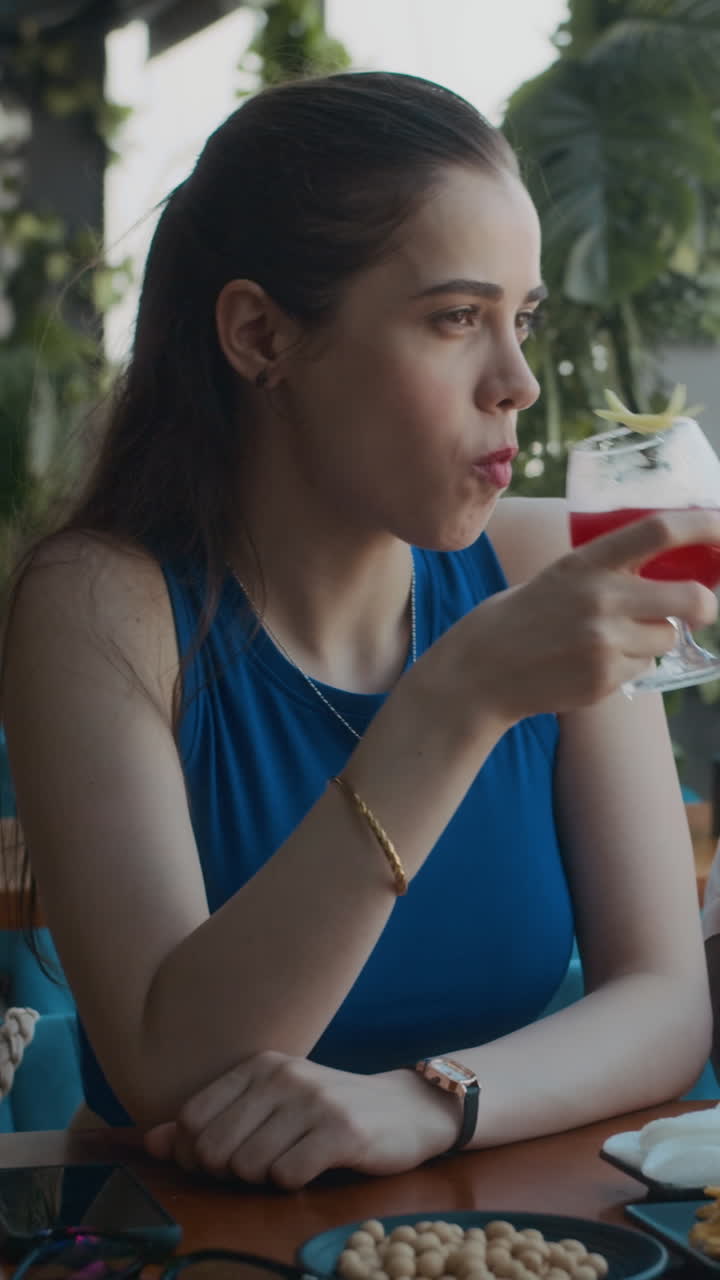 Young Woman Drinking Cocktail at Table with Snacks in Cafe
