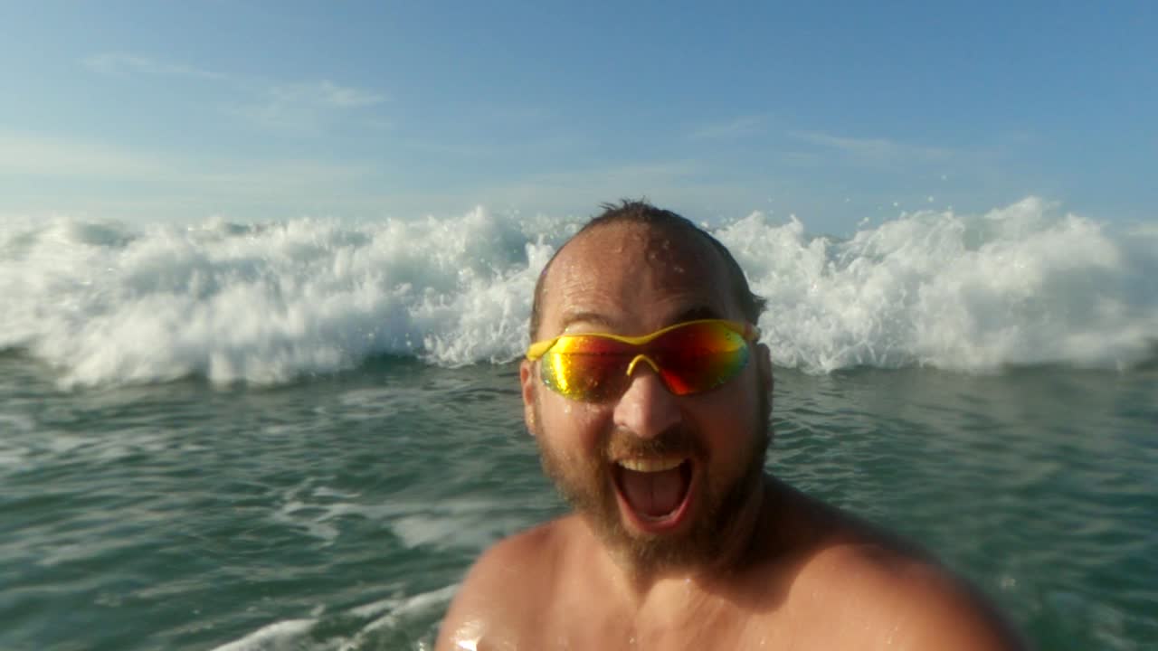 Uomo attivo che si diverte a farsi bagnare dalle grandi onde marine che gli si infrangono in testa.
