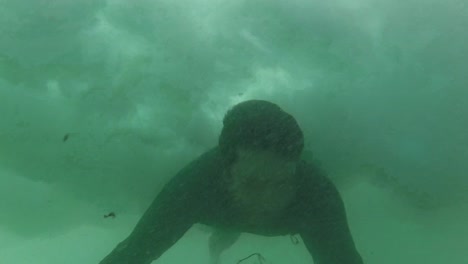 underwater, slow motion, close up: unknown surfer dude paddling on cool surfboard to catch a wave