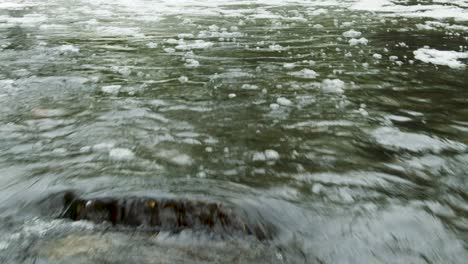 Low to the water flight over a shallow clear water forest river with a vertical tilt revealing a small waterfall
