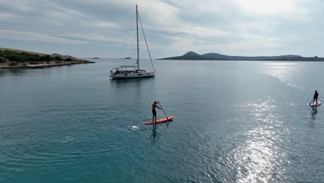 standup paddleboarding in the sea near the yacht. - aerial shot