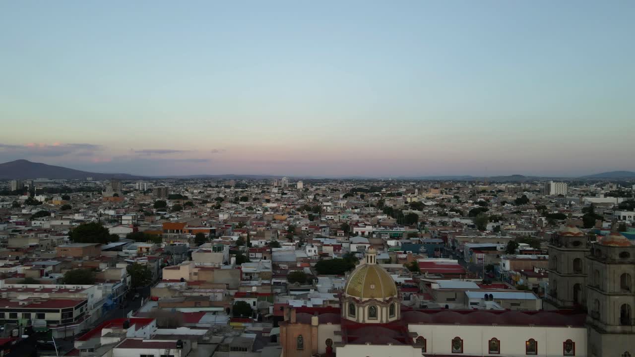 Discesa aerea statica su Guadalajara che mostra gli edifici della città, la chiesa e l'espansione urbana durante un limpido pomeriggio al crepuscolo. Registrato in 4K Apple ProRes 422.