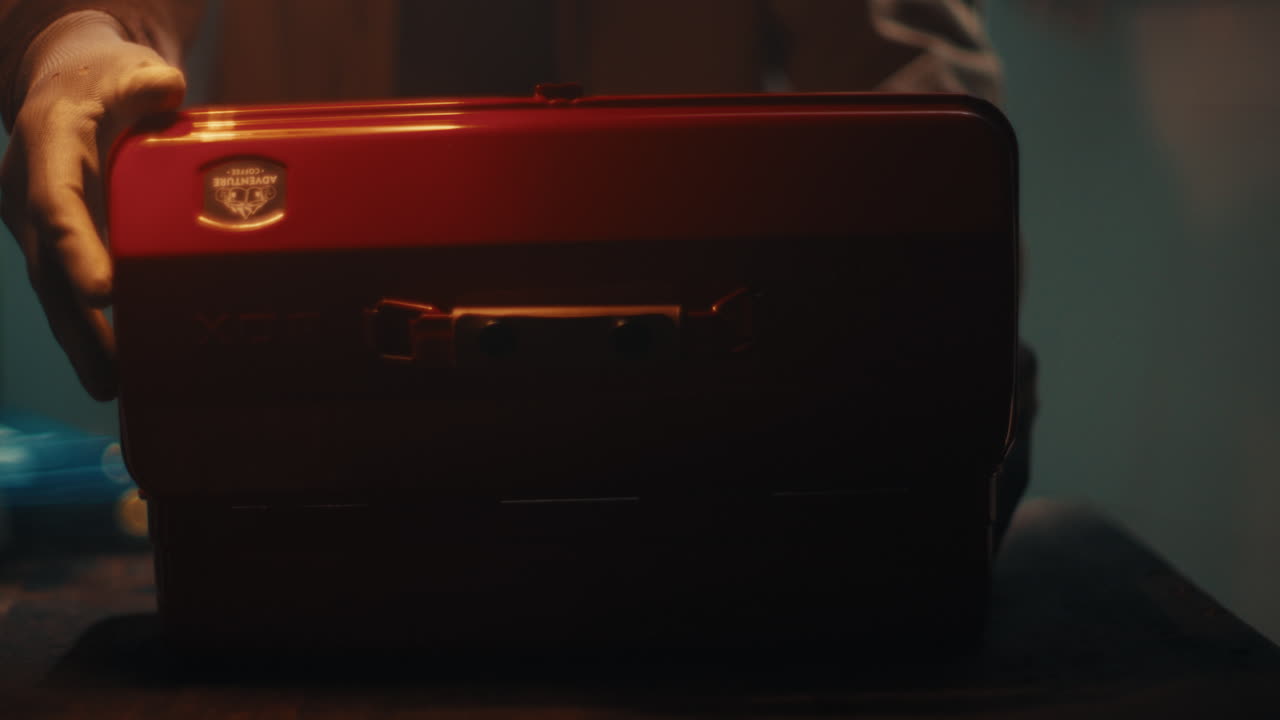 Mechanic placing red metal toolbox on work surface inside dim workshop environment, open and return from industrial chest