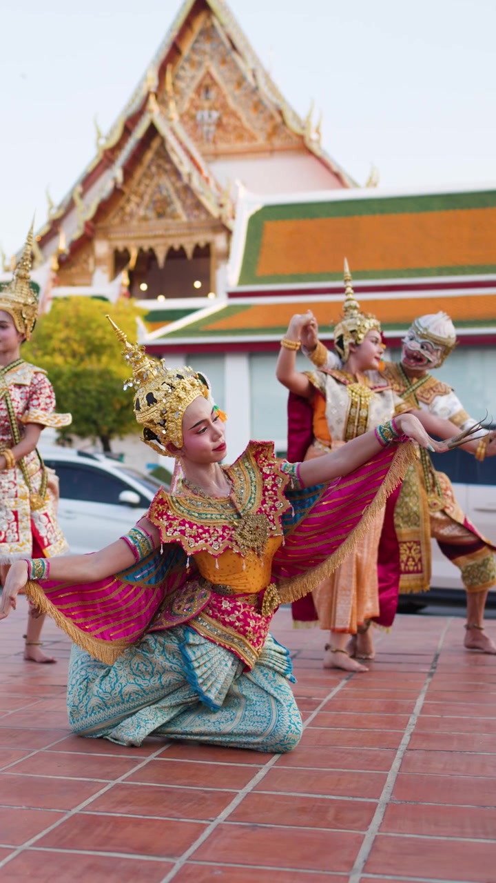Artistas tailandeses con elaborados trajes dorados bailan con gracia frente al patio de un histórico templo de Bangkok.