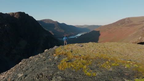 Mountain-walker-standing-on-cliff-edge-with-flight-towards-then-over,-revealing-shadowed-valley-in-early-morning-autumn-sunshine