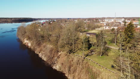 Lettische-Ländliche-Landschaft-Mit-Einem-Gewundenen-Fluss-In-Der-Nähe-Der-Stadt-Lielvarde,-Blattlosen-Bäumen,-Luftaufnahme-Von-Oben,-Fluss-Daugava,-Sonnigem-Frühlingstag,-Freizügiger-Weitwinkelaufnahme,-Die-Sich-Rückwärts-Bewegt,-Kamera-Nach-Oben-Geneigt