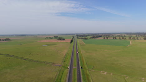 Aerial zoom in drone flying over a green field with a route and the sky with some clouds. A truck passing on the road