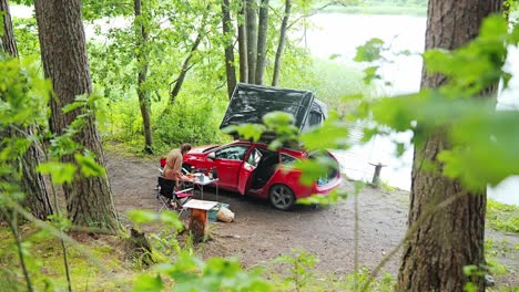 peaceful solo camping by forest lake as woman cooks beside red rooftop car