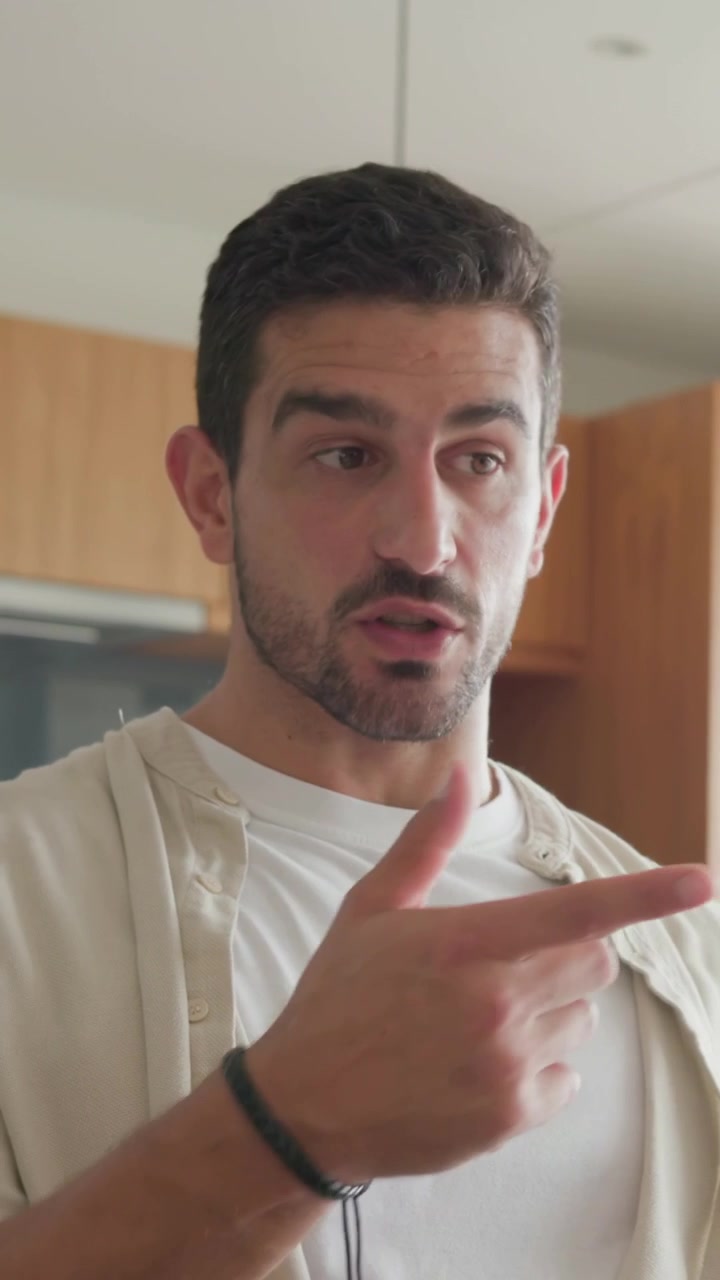 Video verticale: Un uomo si ferma per controllare un tablet in cucina, leggendo e toccando lo schermo e gesticolando verso un ascoltatore.
