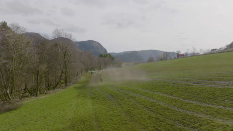 tractor drives next to bare trees spraying fertilizer on green pasture