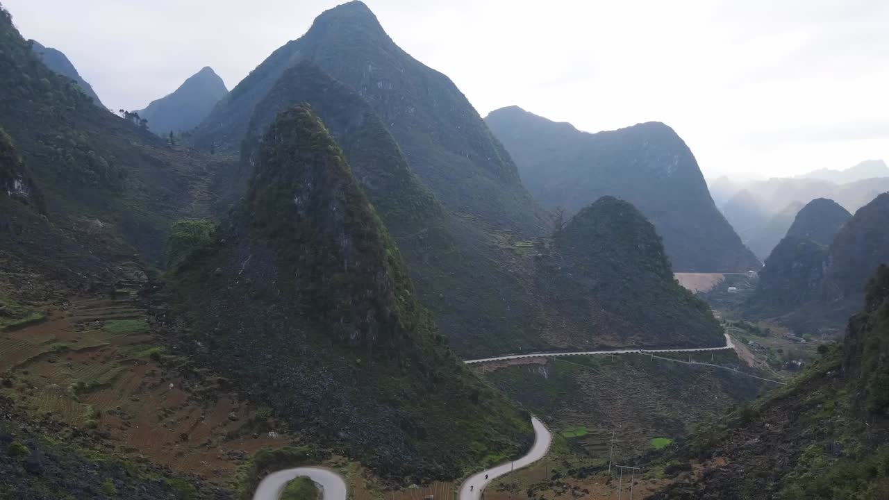 A serpentine road winds through towering karst mountains in northern Vietnam, offering an exhilarating drive through breathtaking valleys and remote, untouched natural landscapes.
