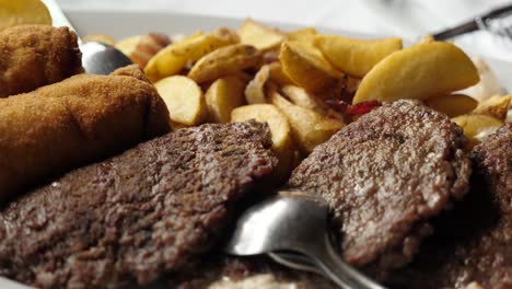 plato de carne con papas hechas a mano, queso enrollado y empanizado, salsa de ajvar, cebolla y limón