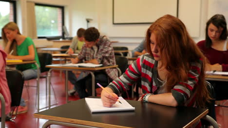 Estudiantes-Tranquilos-Sentados-En-Un-Salón-De-Clases-Y-Tomando-Notas