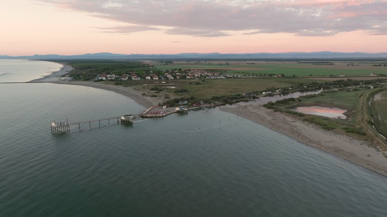 vista aérea en cámara lenta de cabañas de pesca a orillas del estuario al atardecer, máquina de pesca italiana, llamada "trabucco" ravenna cerca del valle de comacchio
