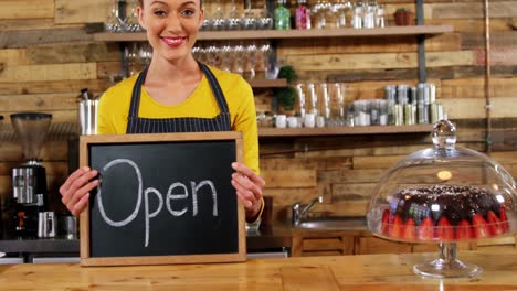 lächelnde kellnerin zeigt schiefer mit offenem schild