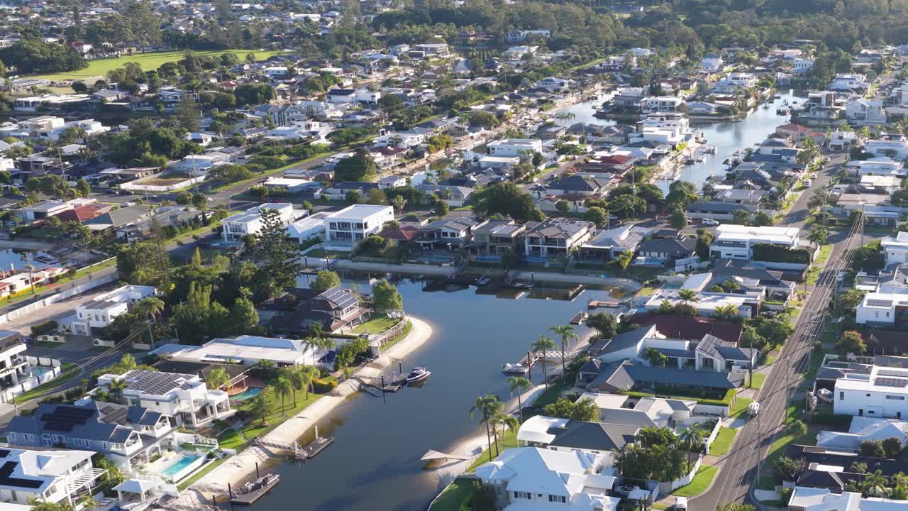 Aerial footage captures canal-side homes in Gold Coast, Australia, under bright daylight, showcasing a serene residential area