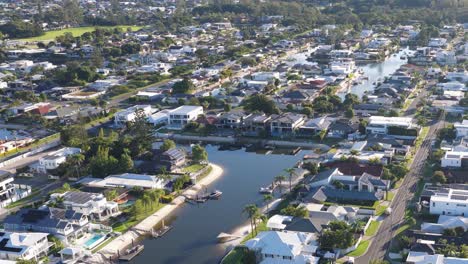 aerial footage captures canal-side homes in gold coast, australia, under bright daylight, showcasing a serene residential area